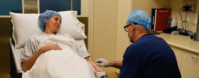 An anaesthesiologist in blue scrubs prepares a patient for surgery. 