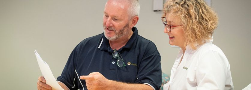 A man and a woman looking at a piece of paper and smiling.